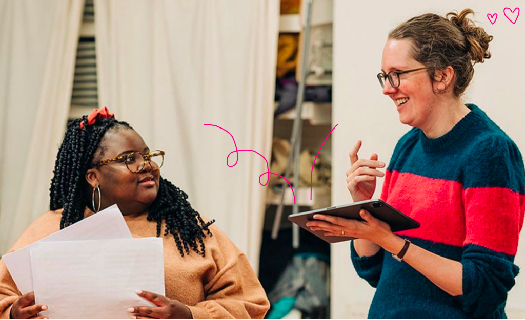 image of Rosemary Linnell holding an iPad and talking to a black female-presenting person holding two sheets of paper, photo credit: Alice Boagey